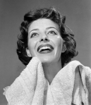1950s smiling woman drying face with towel looking up